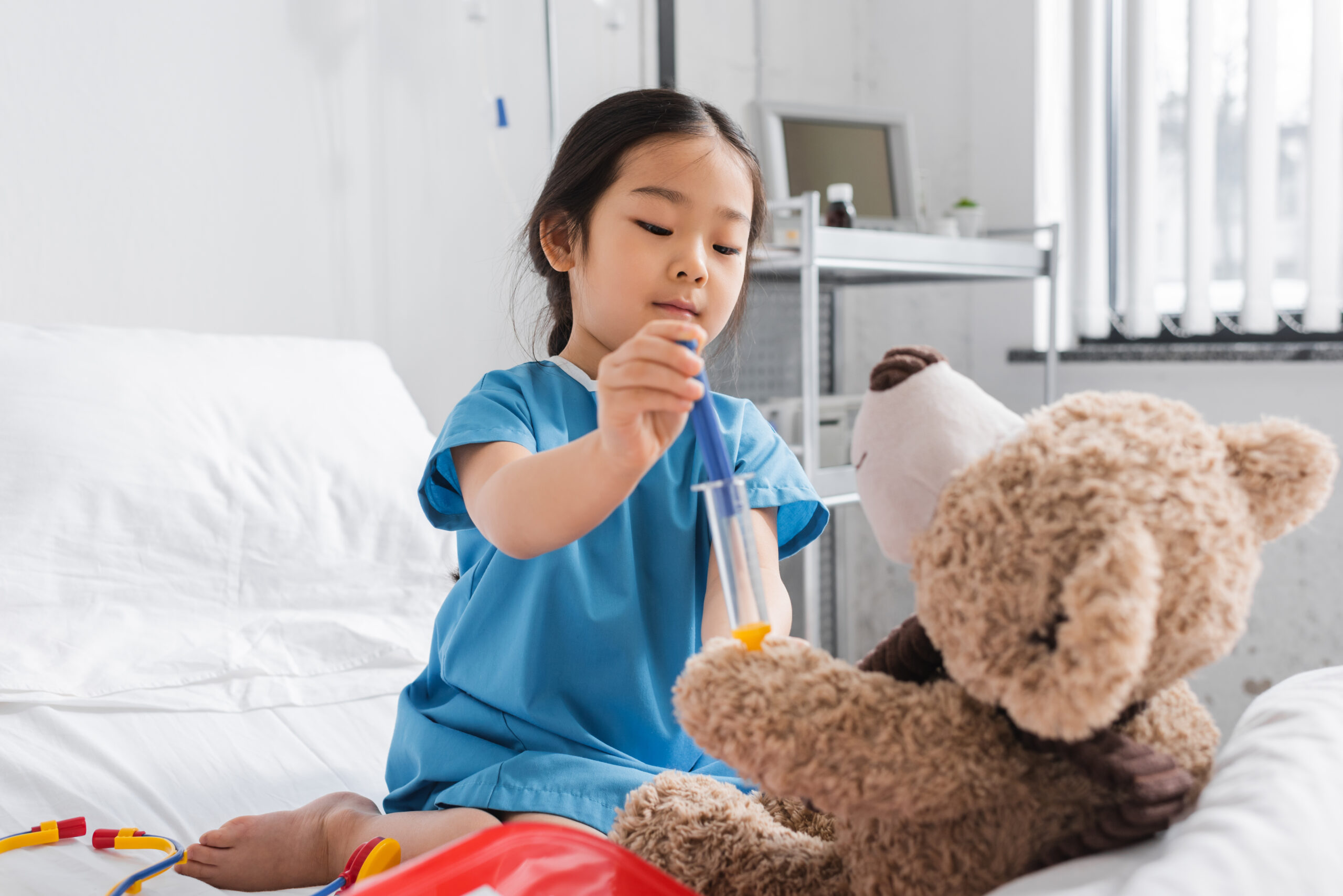 Little girl in hospital bed examining her teddy bear with a medical kit