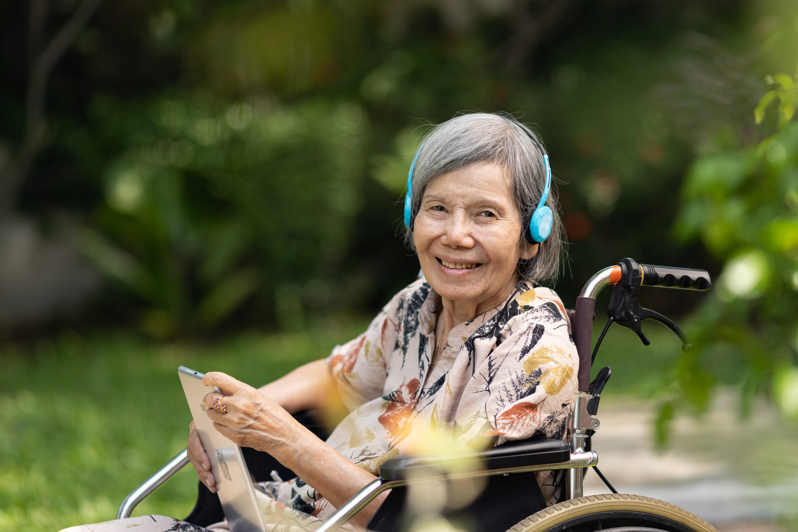 Older woman in wheelchair on her ipad with headphones smiling