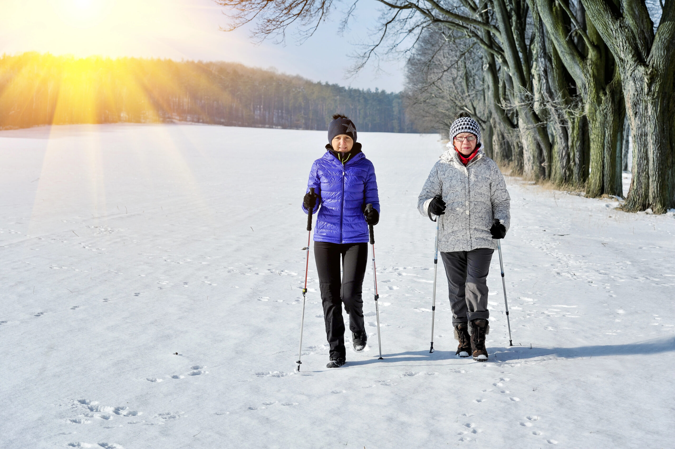 Two older women walking in the snow with nordic poles